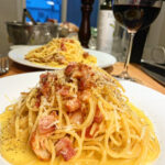 two plates of pasta carbonara with a glass of red wine