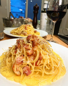 two plates of pasta carbonara with a glass of red wine