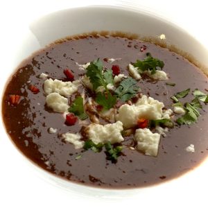 Bowl of black bean soup garnished with cheese & cilantro