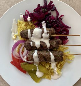 kibbeh on a plate with spiced rice and white sauce and pickled vegetables