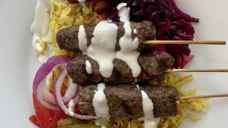 kibbeh on a plate with spiced rice and white sauce and pickled vegetables
